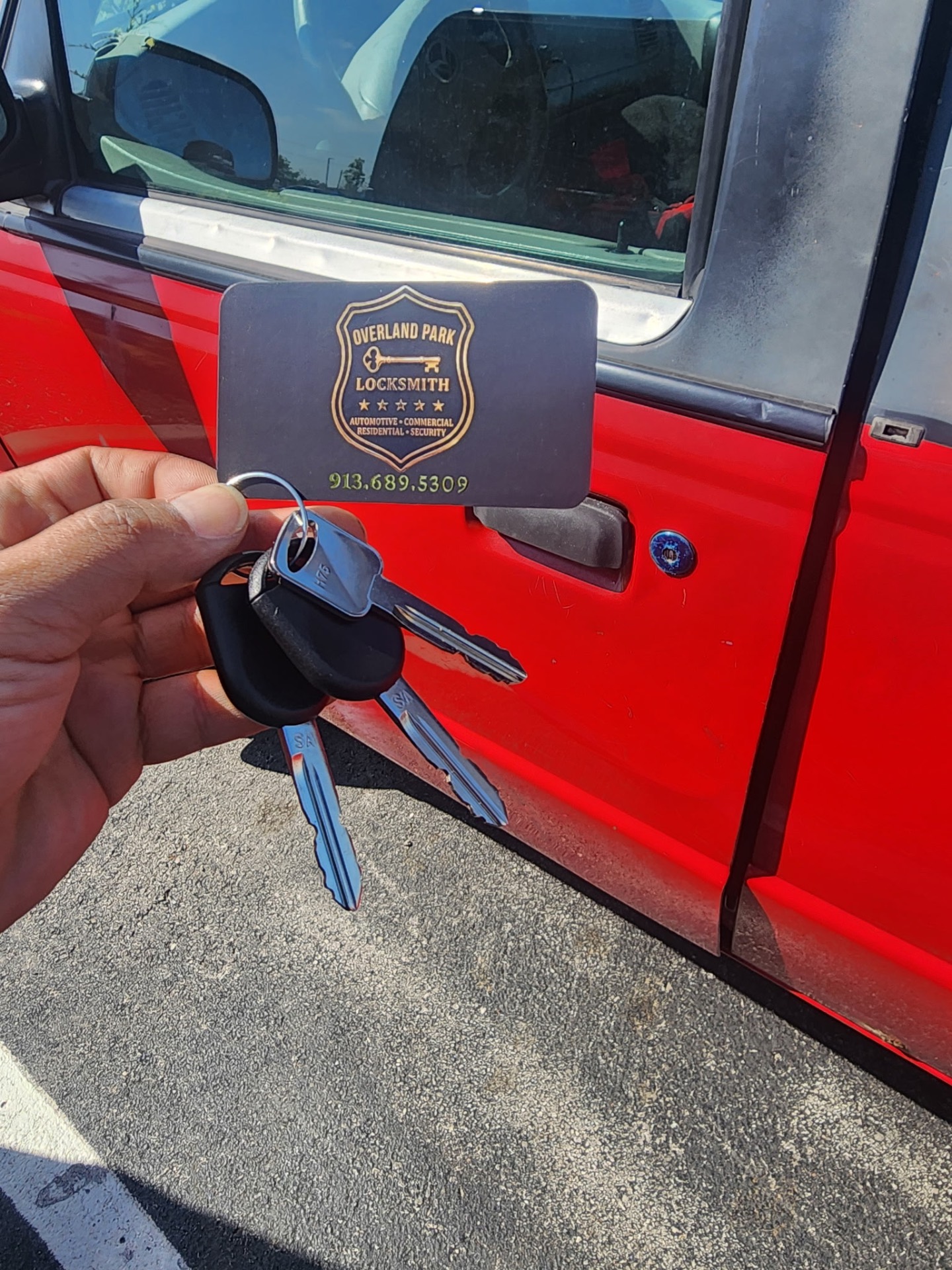 Freshly cut and programmed car keys held next to a red vehicle by Overland Park Locksmith